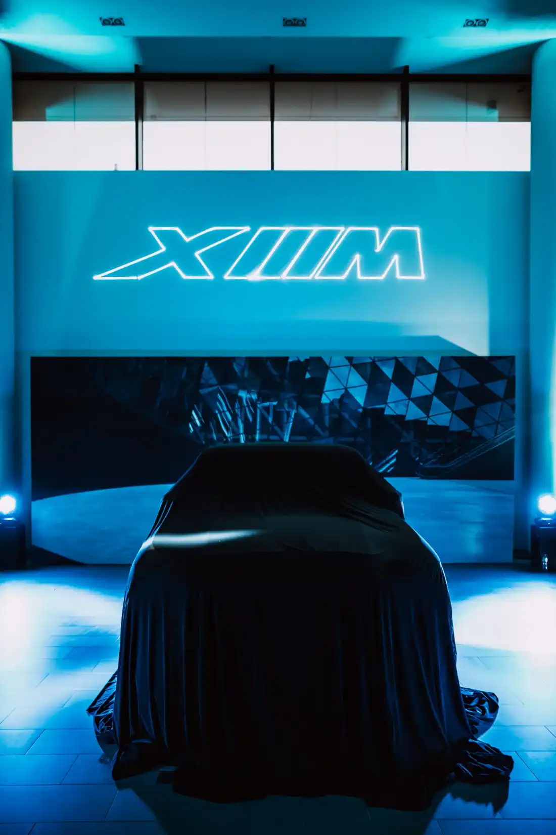 A covered car in front of an LED wall, the XM logo written in light above it